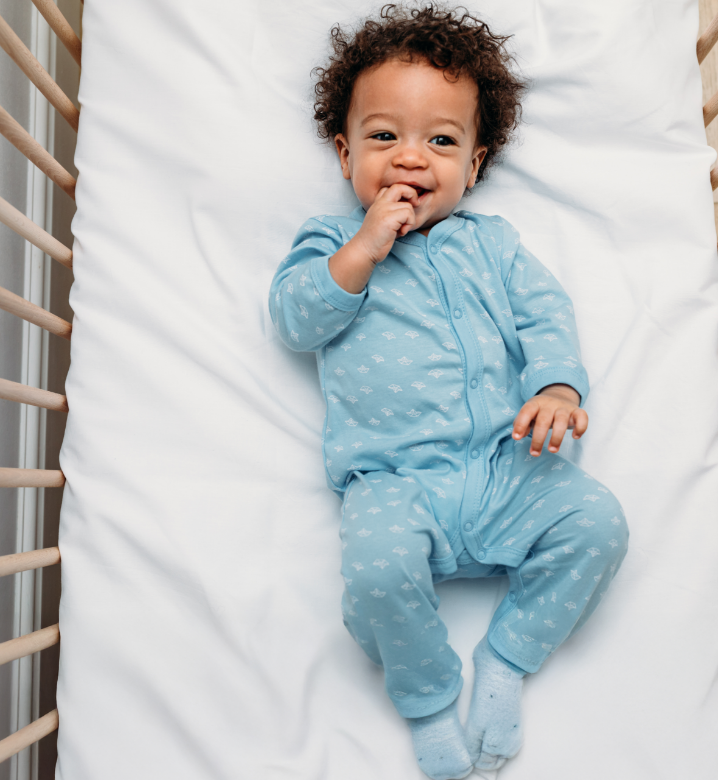 Baby in a blue onesie with white patterns lying on a white blanket.